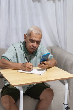 Kıdemli adam konsantre oluyor, evde akıllı telefondan notlar alıyor.
