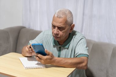 Usta adam akıllı telefonla konuşurken konsantre oluyor ve not almaya hazırlanıyor.