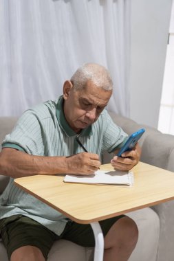 Kanepede oturan, not defterine yazan ve cep telefonuna danışan kıdemli bir adam.