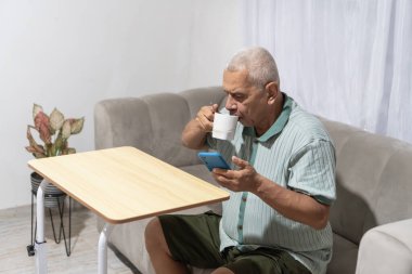 Son sınıf öğrencisi kanepede dinleniyor, kahve içiyor ve akıllı telefonuna bakıyor.