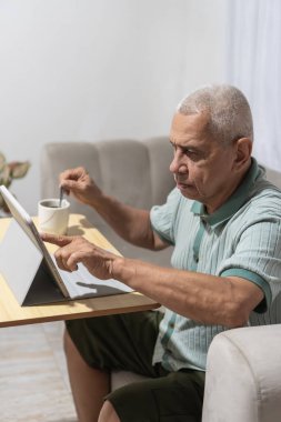 Yoğunlaşmış kıdemli adam evde kahve karıştırırken tabletle etkileşime geçiyor.