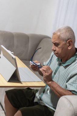 Evde portatif bir masada tablet kullanmaya hazırlanan yaşlı bir adam göz temizliği yapıyor.