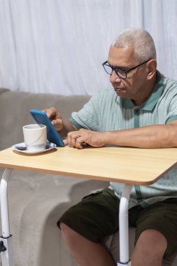 Üst düzey bir adam bir fincan kahveyle masada otururken akıllı telefon kullanıyor.