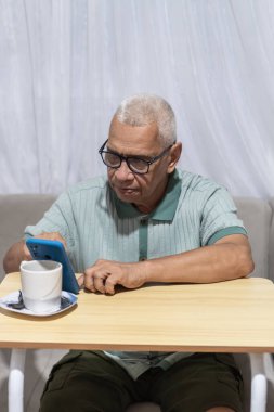 Üst düzey adam içeride kahve içerken iletişim ve teknoloji için akıllı telefon kullanıyor.