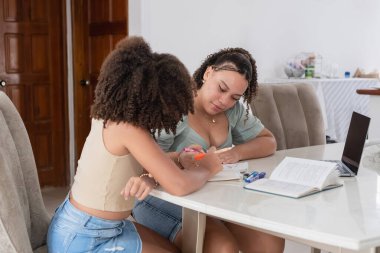 İki genç bayan ders çalışıyor, biri diğerinin ödevlerine yardım ediyor.