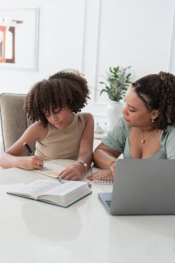 Büyük ablası küçük kız kardeşine destek oluyor ve bir masada dizüstü bilgisayarla öğreniyor.
