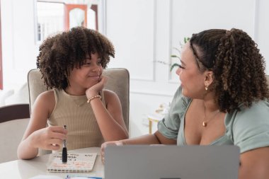 Yetişkin bir kadın, genç bir kıza danışmanlık yapıyor. Masada dizüstü bilgisayarla ders çalışıyor.