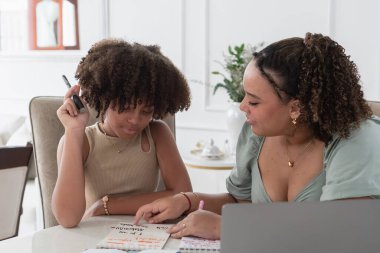 Ablam küçük kız kardeşine masada ödevlerinde yardım ediyor, bir kitabı işaret ediyor.