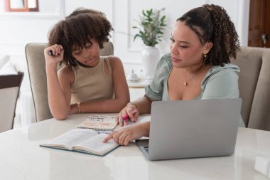 Ders kitabı ve dizüstü bilgisayarla evde ders çalışırken kıza öğretmenlik yapan kadın