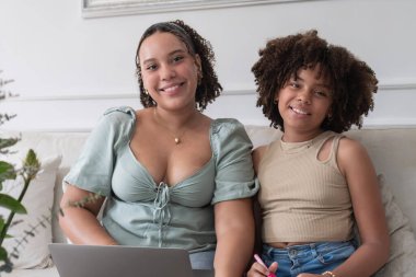 Kız kardeşler gülümsüyor, bilgisayar ve kalemle birlikte öğreniyorlar.