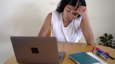 Genç bir kadın evde bilgisayarla çalışırken yorgun ve bunalmış hissediyor.