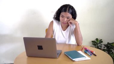 Uykulu ve sıkılmış genç kız evde dizüstü bilgisayarla çalışıyor, esniyor ve uyanık kalmaya çalışıyor.