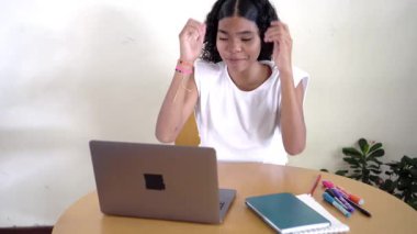 Genç kız öğrenci çevrimiçi öğrenim için bilgisayarını kullanırken heyecan, neşe ve başarı ifade ediyor.