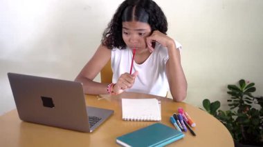 Genç bir kız öğrenci evdeki masasında internetteki görevini tamamlarken derin derin düşünüyor.