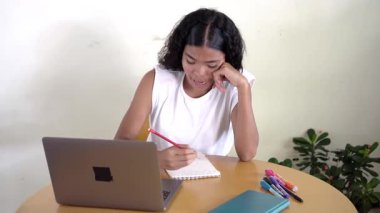 Genç kız bir masada oturmuş online çalışıyor, bilgisayarındaki sanal derste iletişim kuruyor.