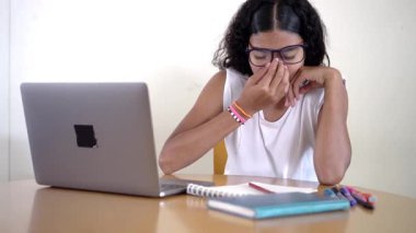 Genç bir öğrenci evde dizüstü bilgisayarla çevrimiçi bir derste uykulu ve yorgun hissediyor.