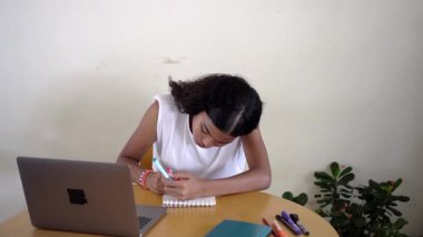 Genç kız öğrenci evde bilgisayarını kullanarak online ders sırasında notlar alıyor ve etkileşime geçiyor.