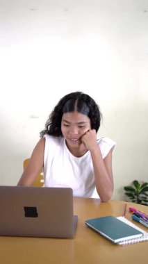 Genç Asyalı kadın evde bilgisayarıyla çalışırken mutlu ve başarılı hissediyor.