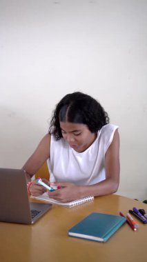 Genç kız dizüstü bilgisayarındaki uzaktan öğrenme seansı sırasında çizimlerini gururla bir deftere gösteriyor.