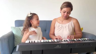 Önemseyen bir anne, küçük kızına evde piyano çalmayı öğretiyor ve sarılıyor.