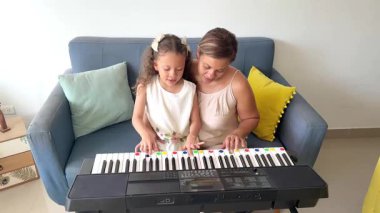 Önemseyen bir anne, küçük kızına oturma odasındaki koltukta nasıl elektrikli piyano çalınacağını öğretiyor.