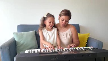 Genç anne, tatlı kızına oturma odasında piyano çalmayı öğretiyor.