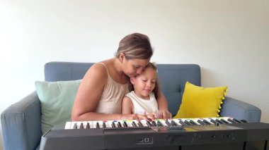 Şefkatli anne tatlı kızına rahat oturma odalarında piyano çalmayı öğretiyor.