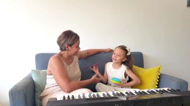 Genç kız ve annesi kanepede oturup eğlenceli ve eğitici piyano derslerinin tadını çıkarıyorlar.