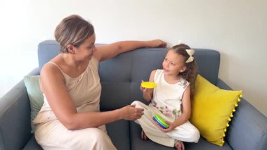 Bakıcı anne, genç kızına koltukta otururken eğitici bir oyuncakla renkler öğretiyor.