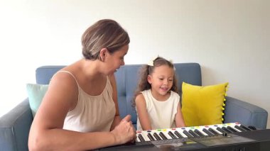 Genç kız annesiyle birlikte oturma odasında elektronik klavye çalmayı öğrenirken eğleniyor.
