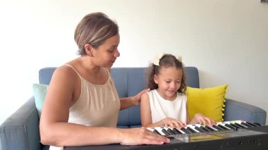 Genç kız, özel müzik öğretmeniyle oturma odasında elektronik klavye çalmayı öğreniyor.