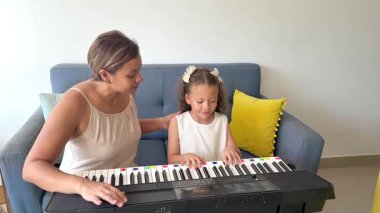 Genç bir kız annesiyle birlikte elektronik klavyede piyano dersi alıyor.