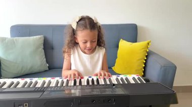 Oturma odasında dijital piyano klavyesinde pratik yapan kıvırcık saçlı tatlı küçük kız.