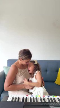 Sevgi dolu anne, tatlı küçük kızına evde kanepede otururken piyano çalmayı öğretiyor.