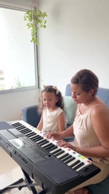 Şefkatli anne, küçük kızına rahat oturma odalarında klavye çalmayı öğretiyor.