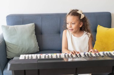 Genç bir kız elektronik klavyede renk kodlu tuşlarla piyano çalışıyor.