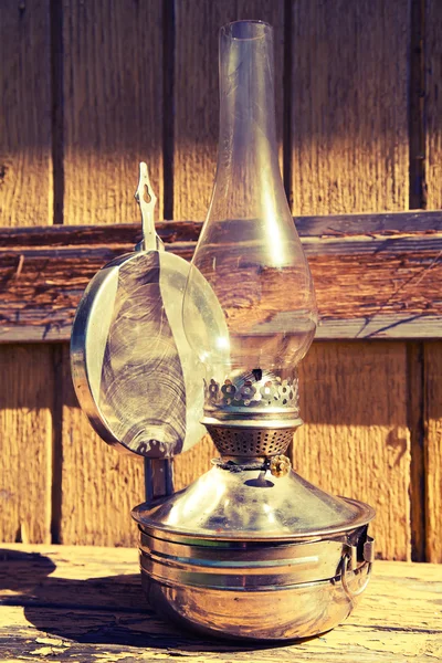 Старая керосиновая лампа стоит на деревянной поверхности, на открытом воздухе, тонизируя — стоковое фото