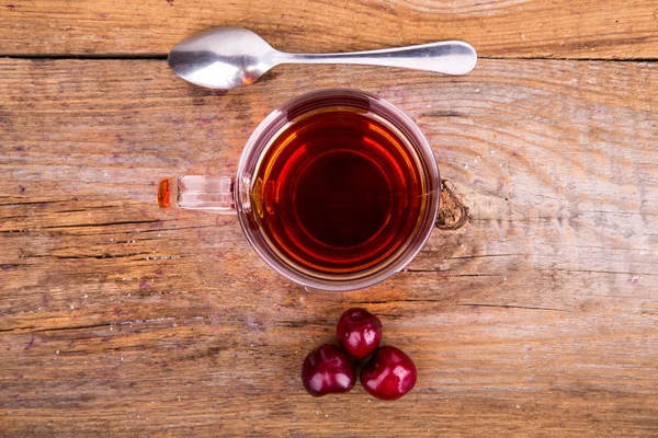 Taza de té, cuchara y cereza dulce sobre un fondo de madera Imagen de archivo