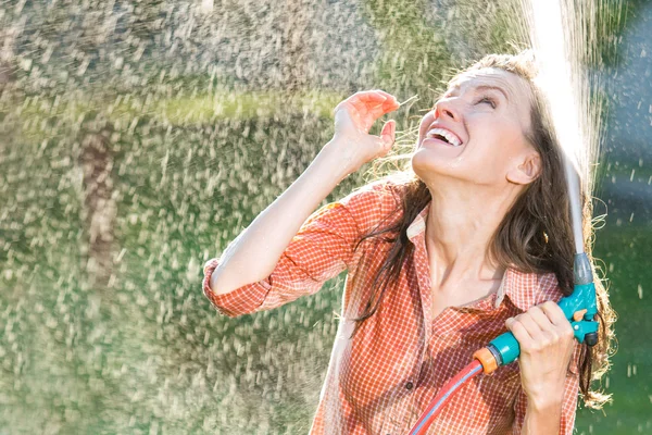 Mulher bonita se divertindo no jardim de verão com mangueira de jardim salpicando chuva de verão — Fotografia de Stock