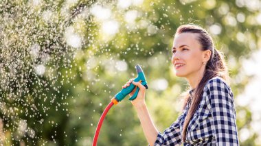 Çiçekleri hortumla sulayan bir kız. Bahar kadını ve bahçe konsepti