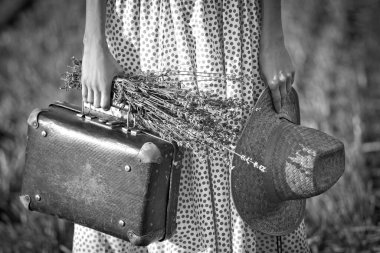 Şapkalı kadın, çiçekler ve bavul.