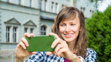 Beautiful woman with a smart phone in green scenery and over old house