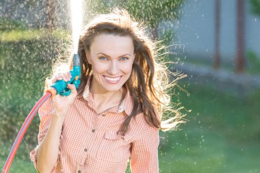 Neşeli genç bir kadın güneşli bir yaz gününde çiçekleri suluyor.