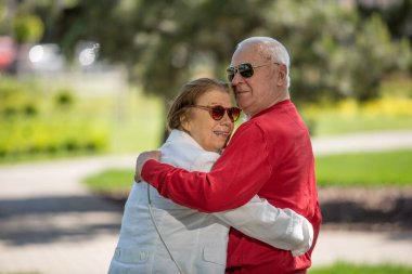 Yaşlı yetişkinler parkta el ele yürüyorlar.
