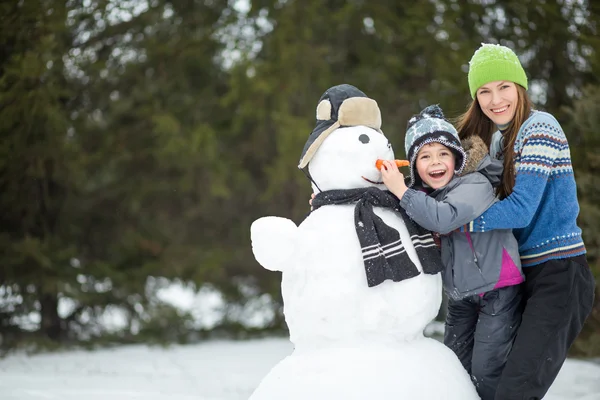 Happy smiling family with snowman — Stock Photo, Image