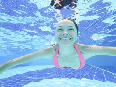 Woman swimming underwater in pool smiling