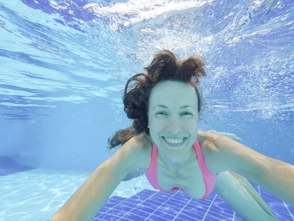 Woman swimming underwater in pool smiling — Stock Photo, Image