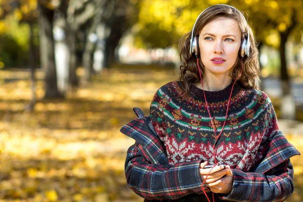 Девушка слушает музыку в осеннем пейзаже золотого парка — стоковое фото
