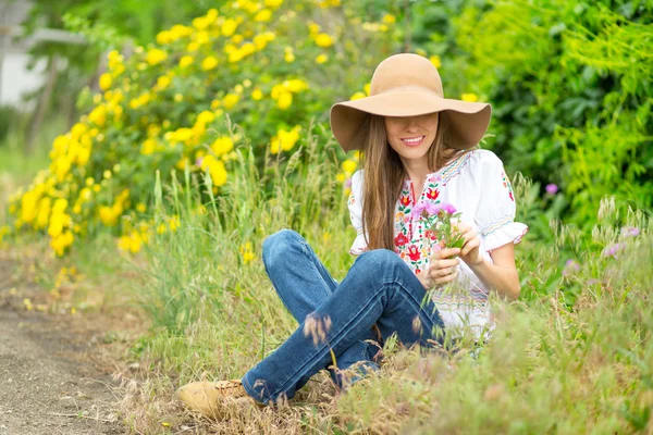 Mulher feliz sentado na estrada rural com fundo de rosas amarelas — Fotografia de Stock