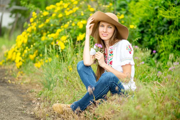 Mujer feliz sentada en camino rural con fondo de rosas amarillas —  Fotos de Stock